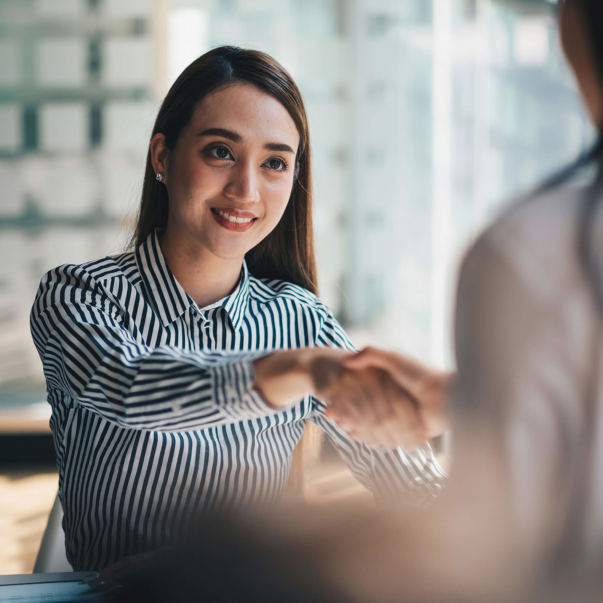 Professional in striped blouse shaking hands with colleague during business meeting in bright office setting