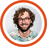 Smiling person with curly brown hair and glasses wearing a light blue shirt against an orange circular background