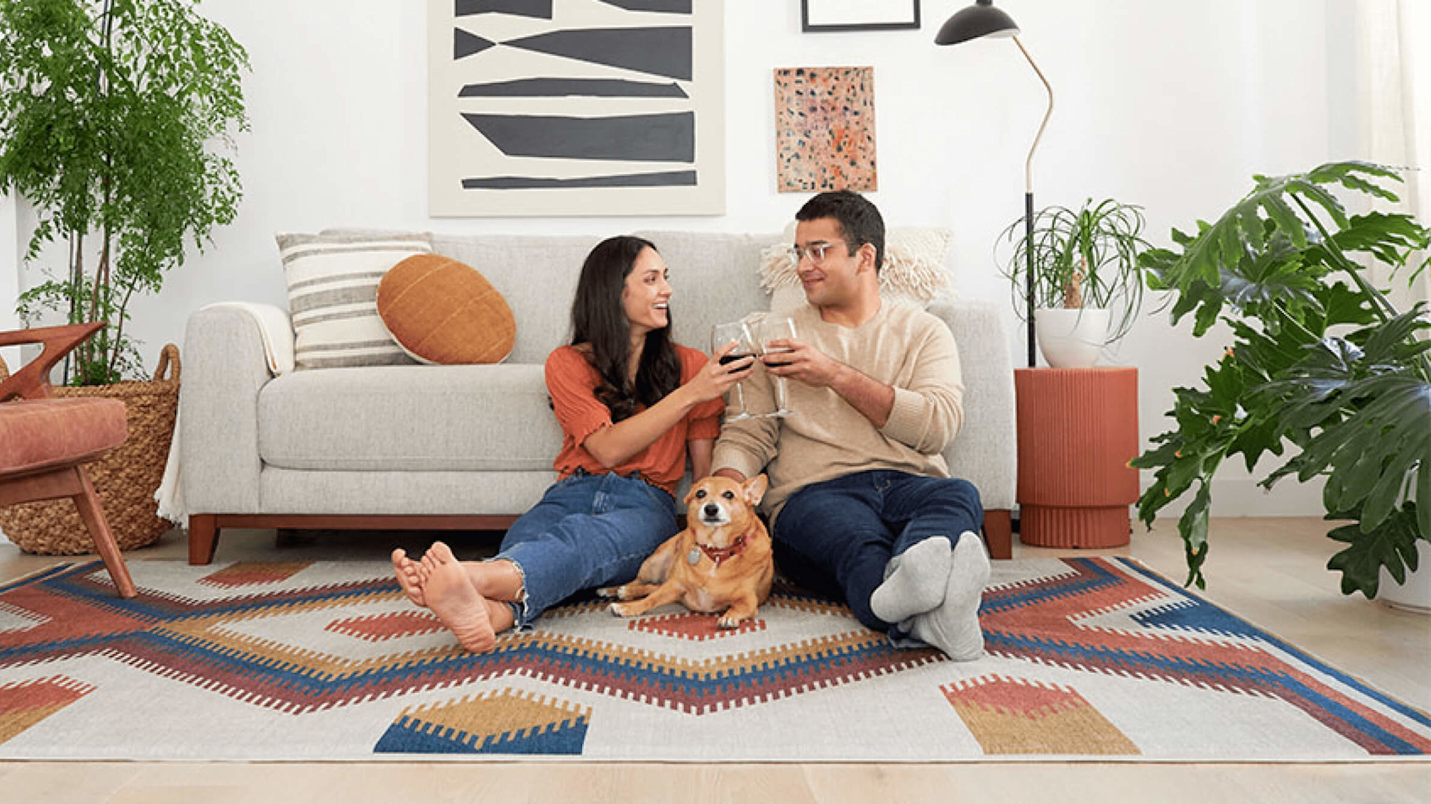 Couple relaxing on a geometric art rug with wine glasses and their golden dog